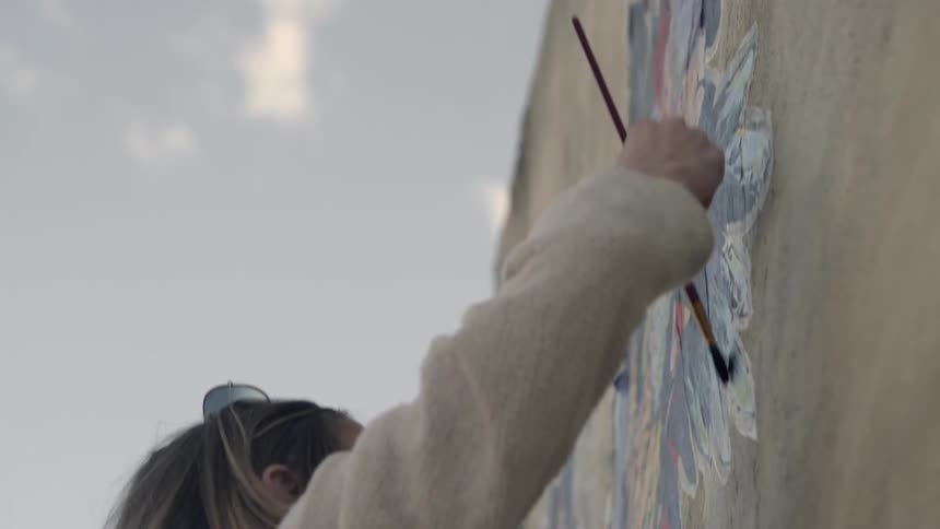 A woman paints a mural on a building