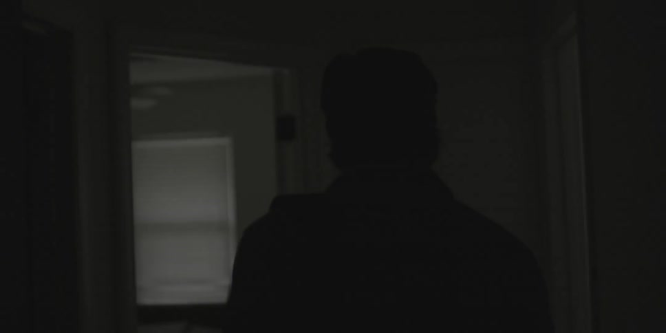 A man walks down a dark hallway in a house