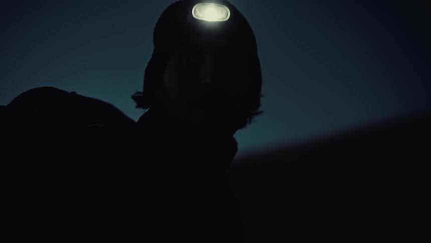 A silhouetted person wearing a headlamp scans the darkness before turning it off