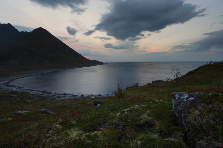A moody time-lapse of a secluded bay surrounded by mountains as clouds drift across the sky at dusk