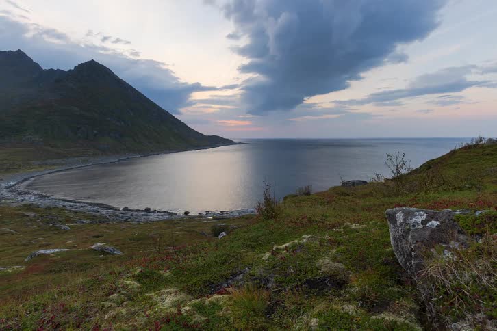 A slow zoom-out reveals a tranquil Scandinavian fjord and mountainside under a dramatic, cloudy sky at dusk