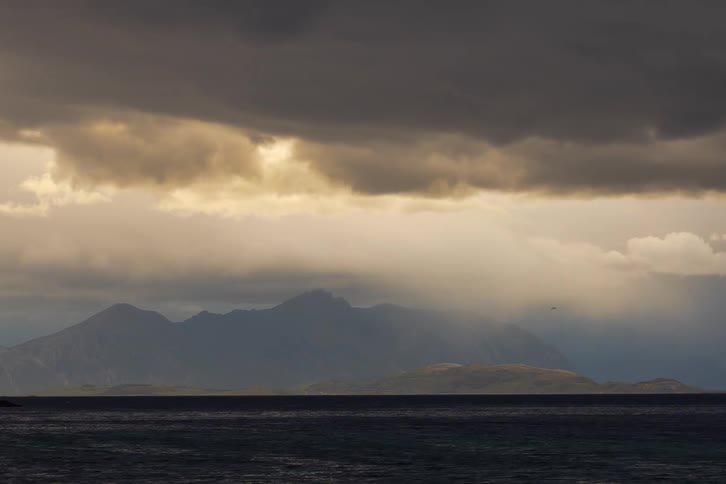 Dark, moody storm clouds drift across the sky in a time-lapse over a vast mountain range and the ocean below