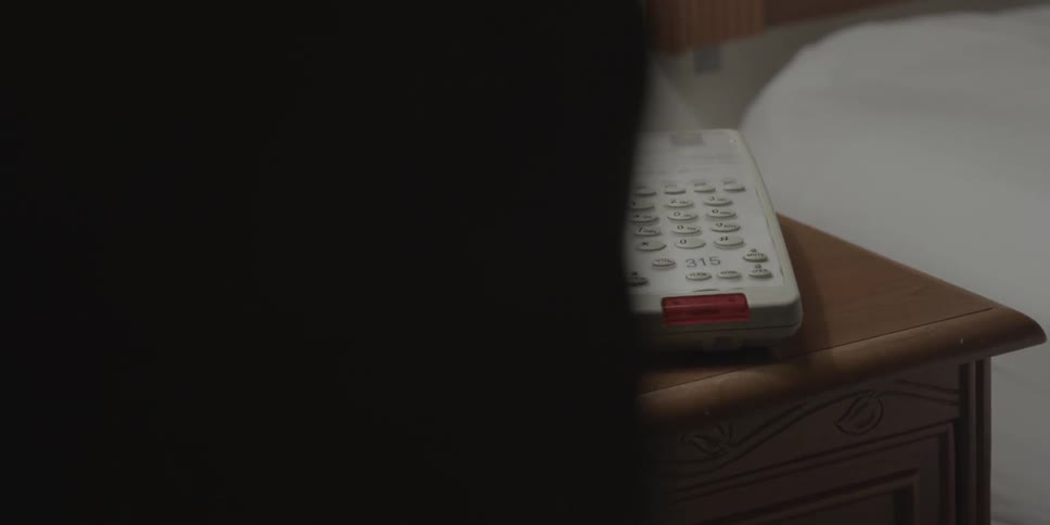 A person stands near a phone on a nightstand