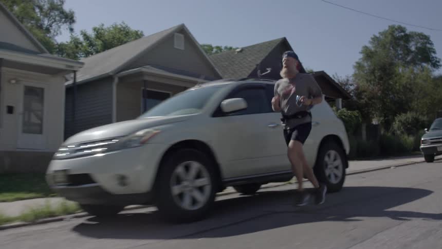 An older man is jogging along a suburban street during the day