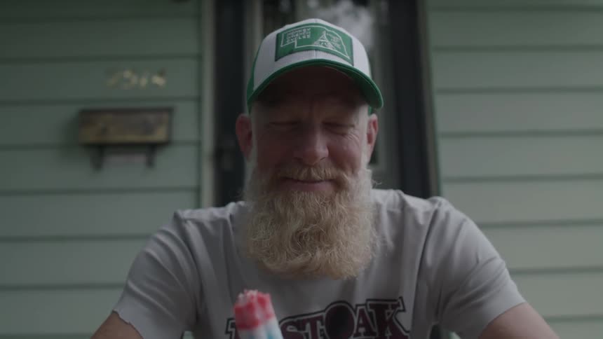 A man eats a popsicle on the front steps of a house