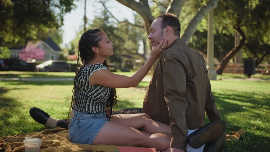 A woman lovingly caresses her partner's face as they enjoy a romantic picnic in a sunny park