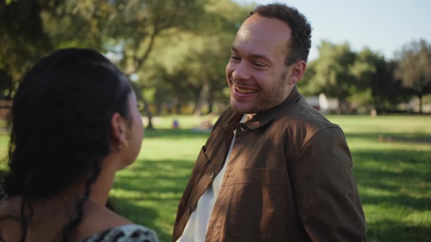 A happy young man laughs and smiles with affection while spending time with his partner in a park on a sunny day
