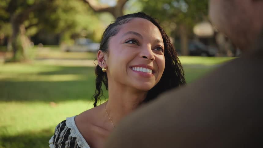 A close-up of a beautiful young woman's face as she looks up and smiles lovingly at her partner during a conversation in a sunny park