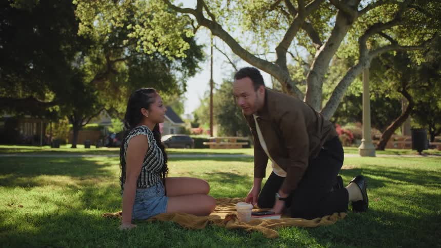 A happy couple has a playful and animated conversation while enjoying a picnic date under a tree in the park