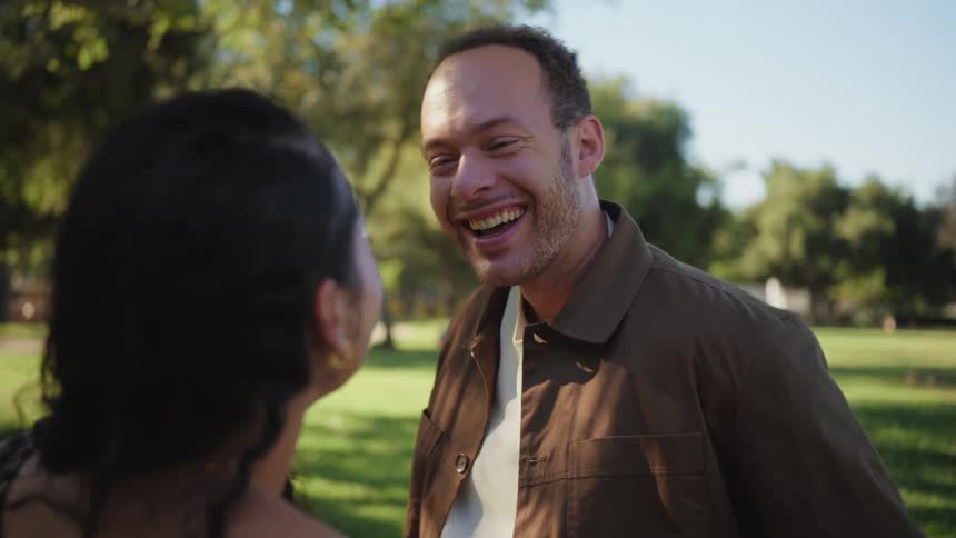 A joyful man in slow motion laughs during a romantic date in a park on a sunny day
