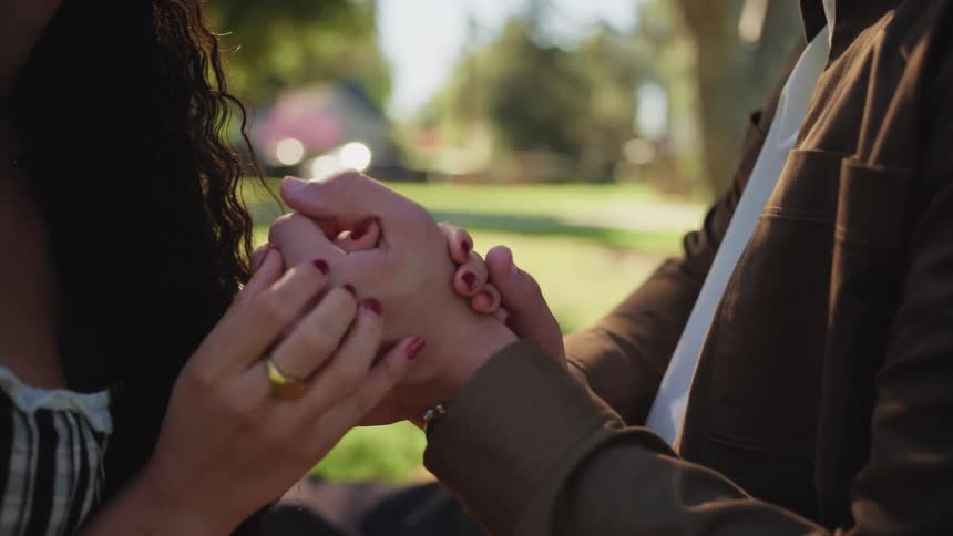 A close-up of a romantic couple holding hands on a sunny day in a beautiful park