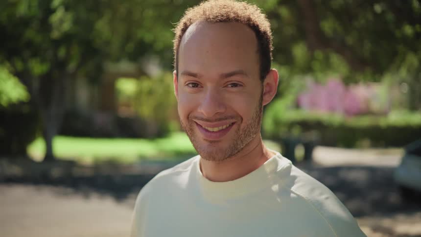 A handsome young man looks up and gives a charming smile to the camera on a sunny day in a suburban neighborhood