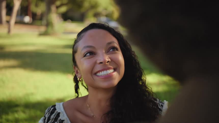 A beautiful young woman smiles lovingly at her partner as they share a romantic moment in a sunlit park