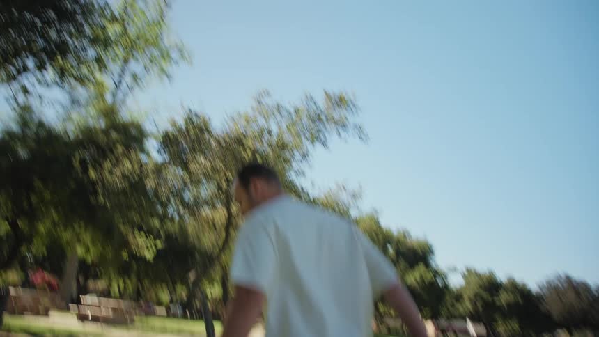 A playful man smiles and runs through a sunny park in a dynamic handheld follow shot