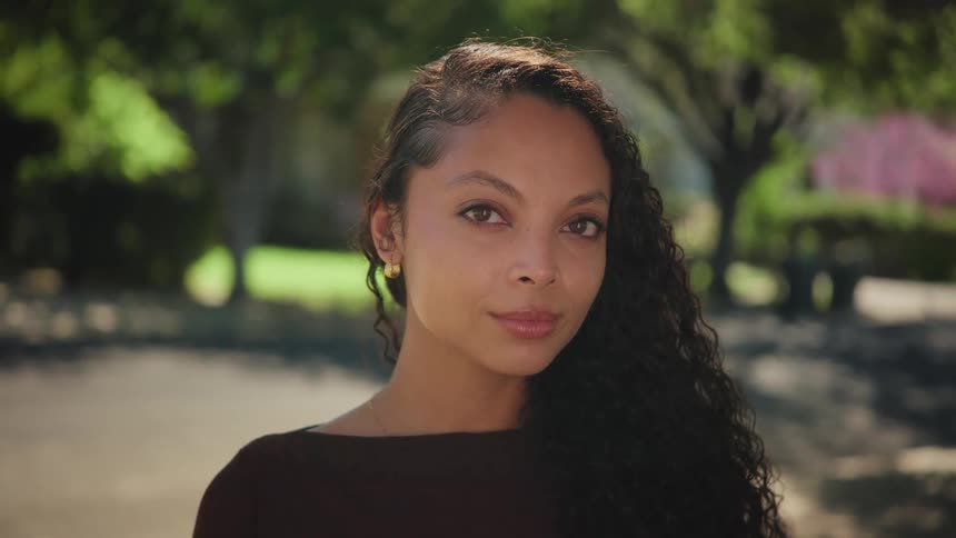 Close up portrait of a beautiful young woman with long curly hair looking directly into the camera in an outdoor park setting