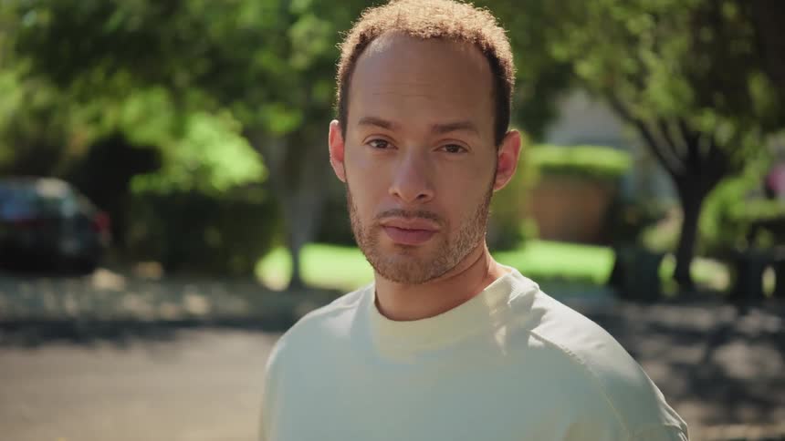 Slow motion portrait of a handsome young man looking directly at the camera on a tree-lined suburban street