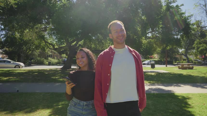 A slow motion shot of a happy young couple holding hands as they walk through a sunny park