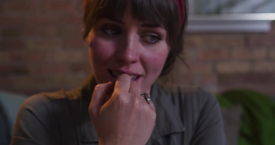 A close-up of a young woman's face as she nervously bites her nails while watching something with suspense and anticipation