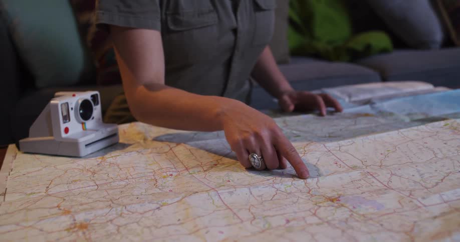 A young woman traces a route with her finger on a paper map as she plans an exciting road trip adventure