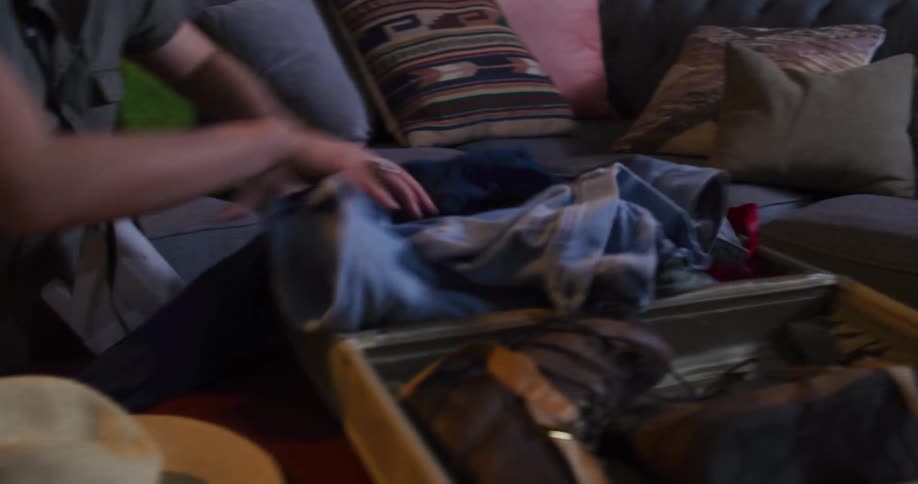 A person packs hiking boots and then a large messy pile of clothes into a vintage suitcase, only to pull the clothes back out again
