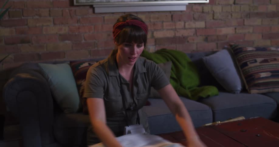 A young woman excitedly unfolds a large paper map on her coffee table, planning her next adventure in slow motion