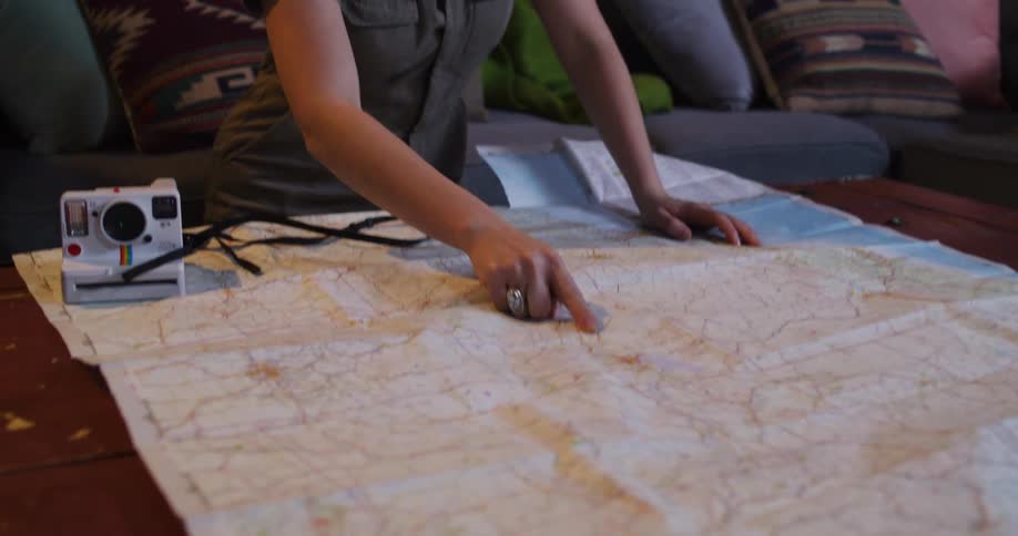 An adventurous woman excitedly plans her next road trip, tracing the route on a large paper map in her living room