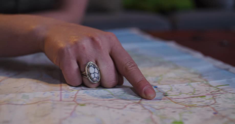 A woman's hand with a decorative ring traces a route along a paper road map to plan her next trip