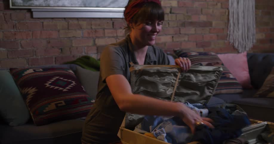 An excited young woman packs her vintage suitcase with clothes and accessories for an upcoming adventure, struggling to close the overstuffed bag