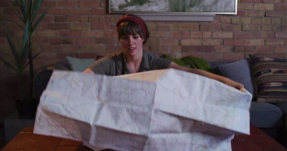 An adventurous woman unpacks a vintage suitcase and unfolds a large paper map across a table to plan her next journey