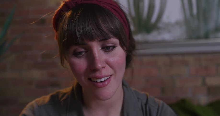 A close-up of an engaged young woman smiling and talking while bathed in warm, soft light