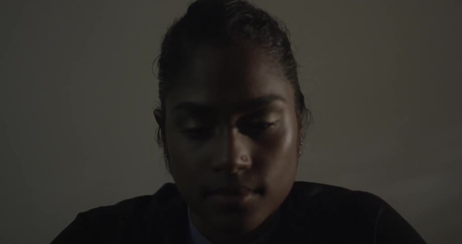 A woman slowly looks down in a dark room