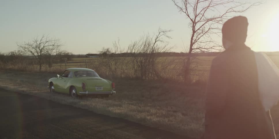 A man walks toward an old karmann ghia parked along a rural road