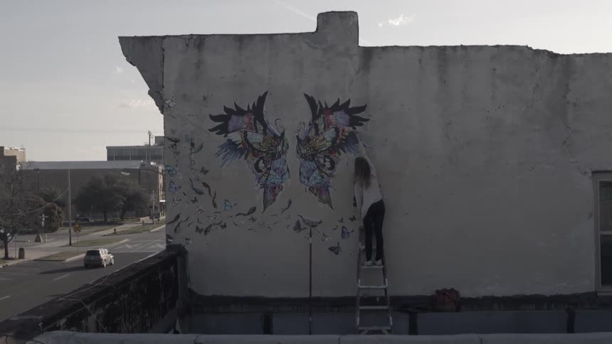 A woman paints a mural on the side of a building