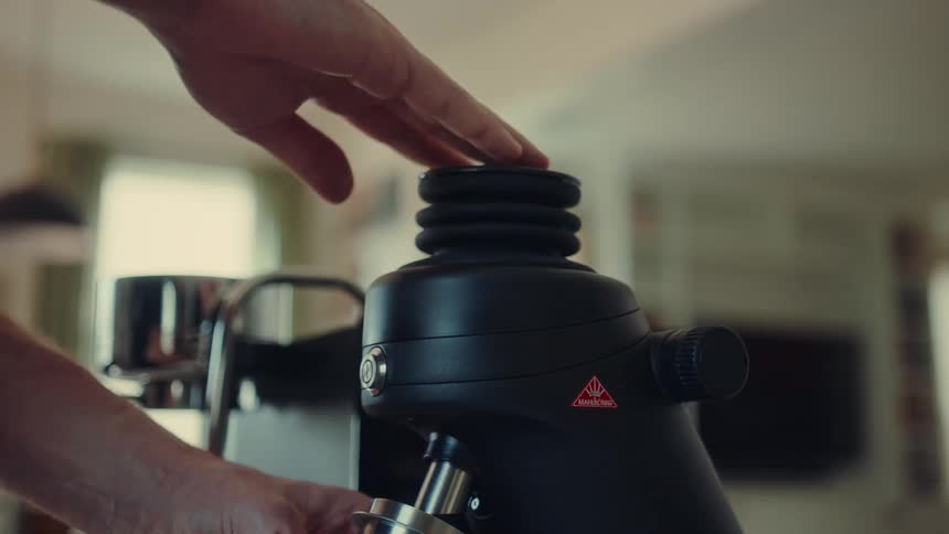 Barista pushes down on the bellows pump of a coffee grinder in a slow-motion, close-up shot