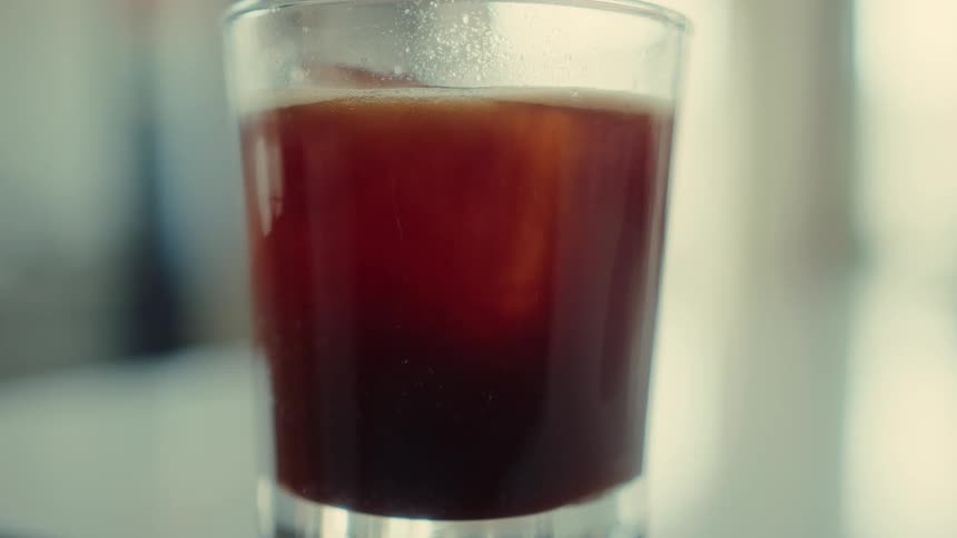 A close-up shot of a glass of iced coffee with ice cubes slowly melting inside