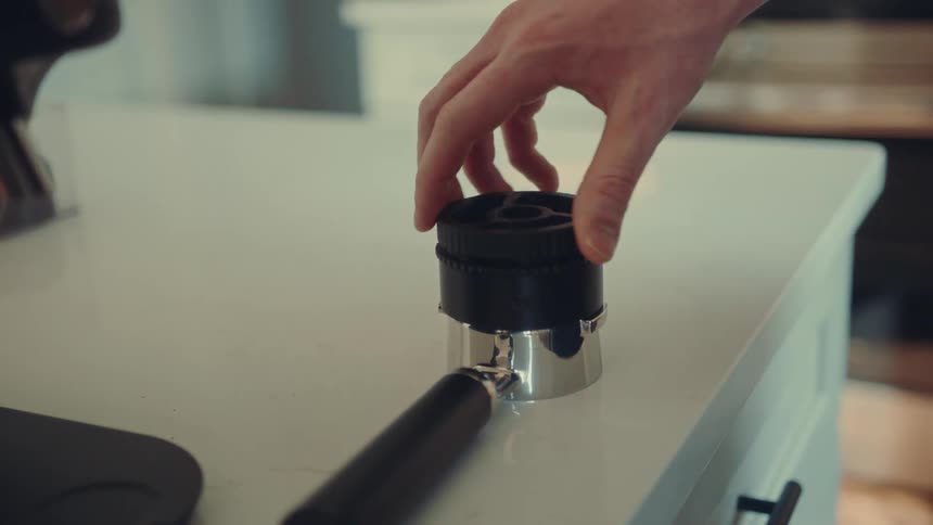 A barista spins a coffee distributor to evenly level the coffee grounds in a portafilter before making espresso