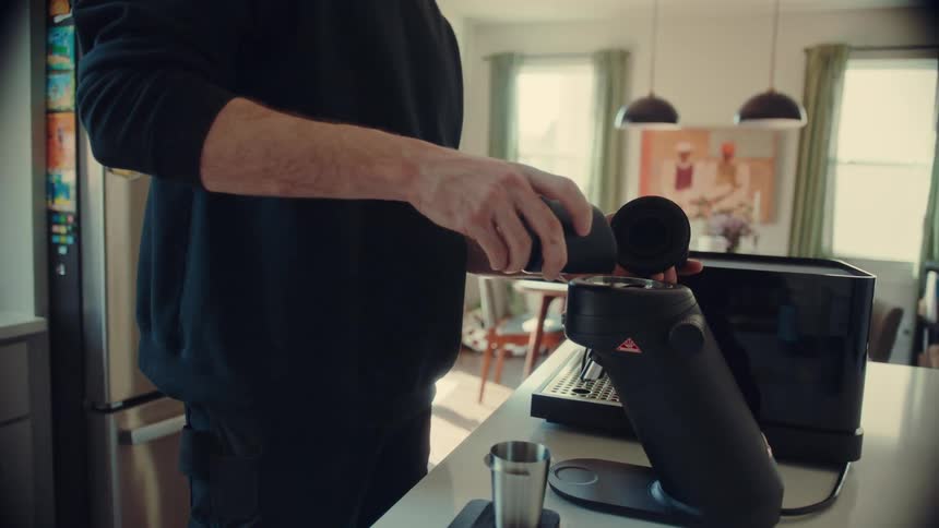 A man prepares to grind fresh coffee beans for his morning espresso in a bright, modern kitchen