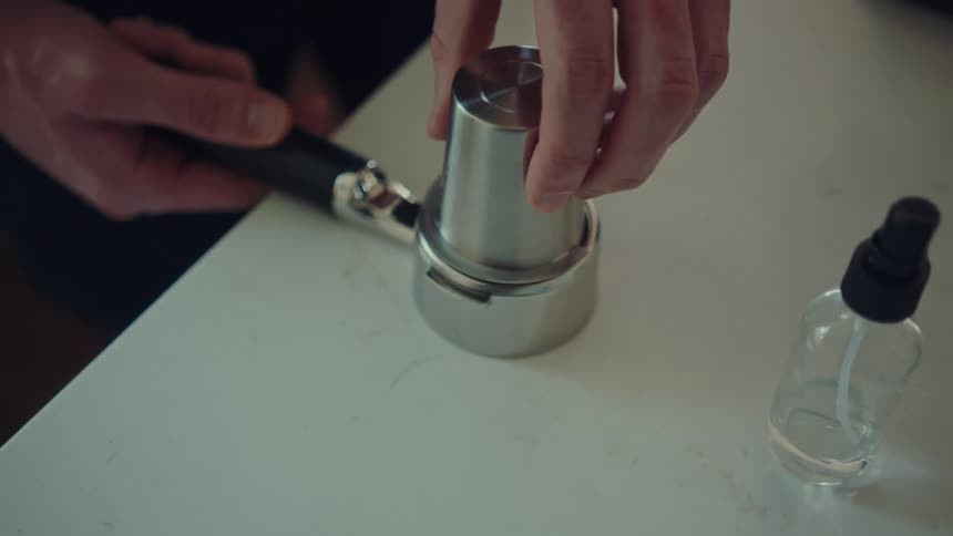 A close-up slow-motion shot of a barista filling a portafilter with fresh ground coffee using a dosing cup