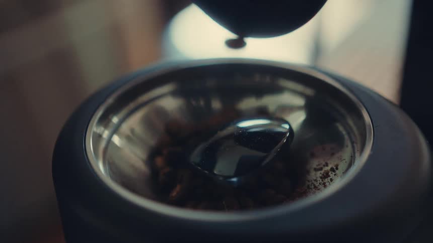 Slow-motion close-up of whole coffee beans falling into an electric grinder to be prepared for brewing