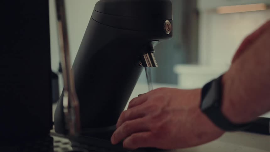 A close-up of a barista grinding fresh coffee beans with a single-dose electric grinder for espresso in a modern kitchen