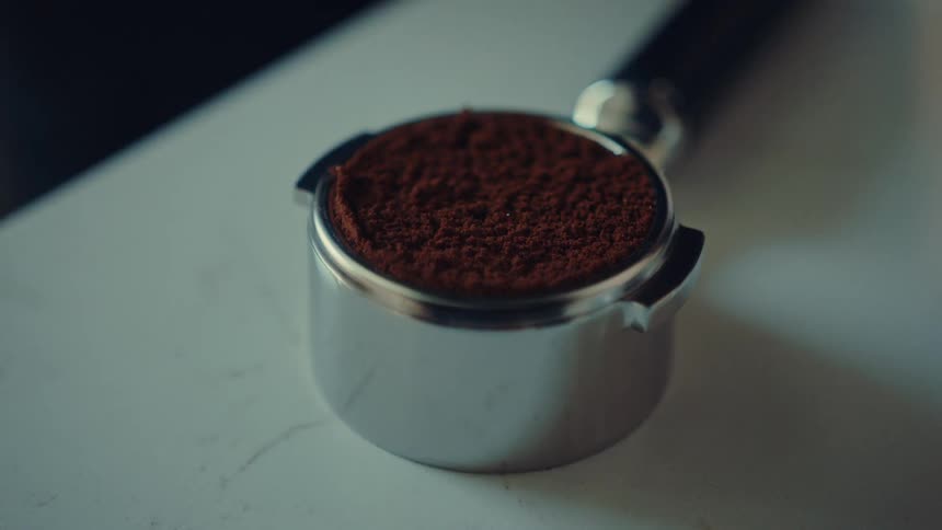 A slow-motion close-up shot of a person grinding fresh coffee beans into a portafilter
