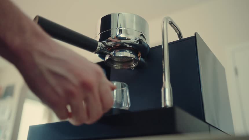 A person prepares a modern espresso machine, locking the portafilter in place and setting a glass to catch the fresh brew