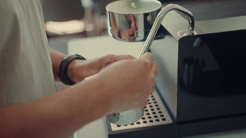 A close-up shot of a person steaming milk in a metal pitcher using a modern coffee machine