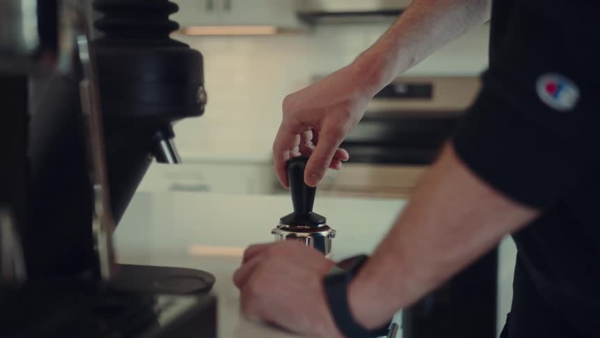 Close up of a barista preparing a shot of espresso by distributing and tamping the grounds before brewing