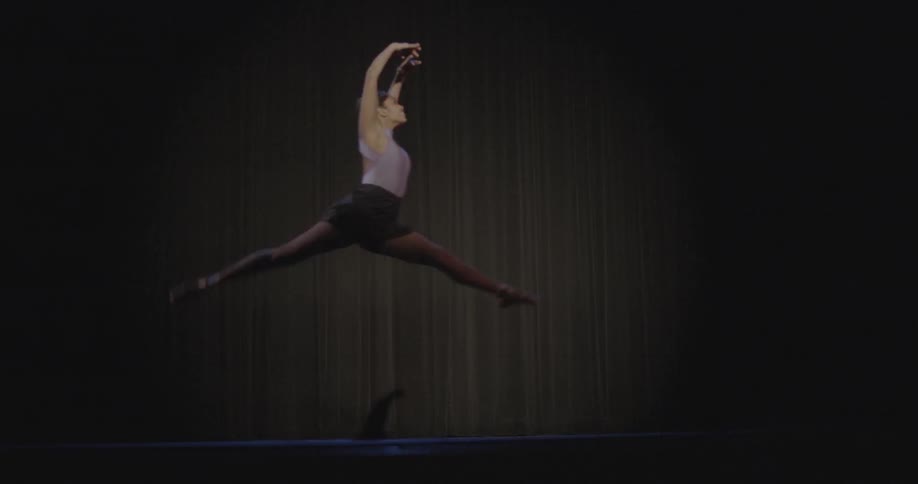 The dark stage has a white curtain and a dancer jumps past