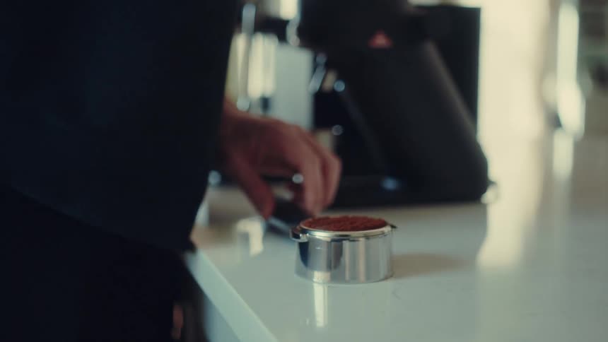 A barista prepares espresso by leveling the grounds with a distribution tool and then tamping them firmly in a portafilter