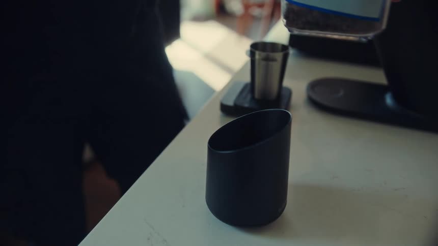 A close-up slow-motion shot of a hand pouring fresh roasted coffee beans into a modern black cup