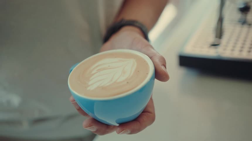 Slow motion close-up of a barista expertly crafting a beautiful leaf design for latte art in a blue cup