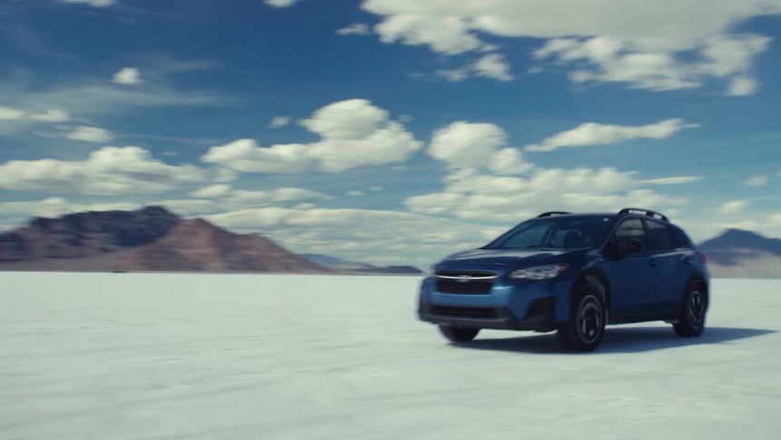 A blue SUV drives across the vast, white landscape of the Bonneville Salt Flats on a sunny day