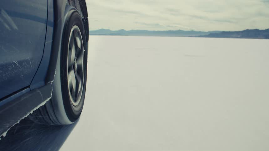 A close-up of a car's tire spinning as it speeds across the vast, white landscape of the Bonneville Salt Flats